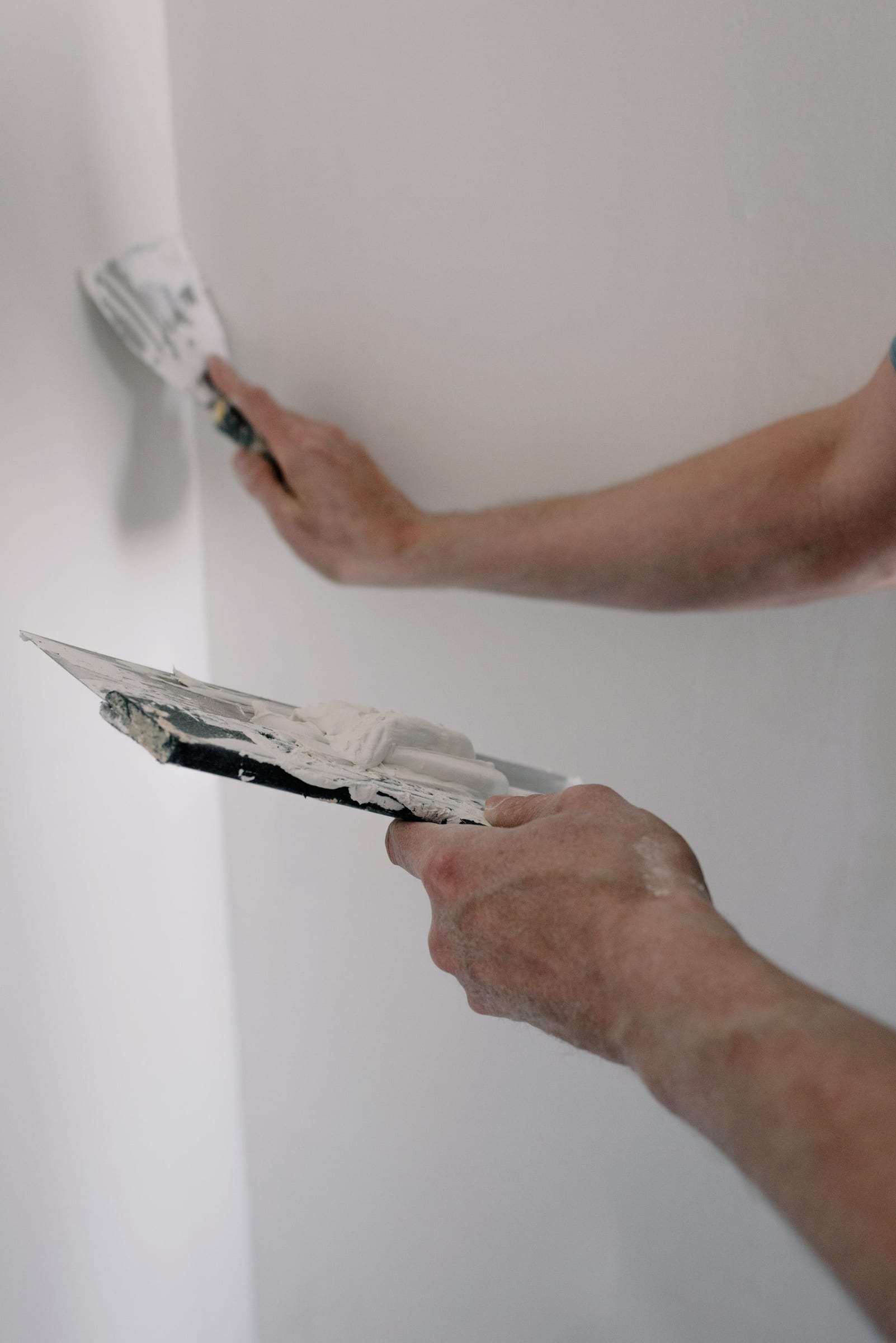 Mains appliquant de l’enduit dans un angle de mur avec deux couteaux