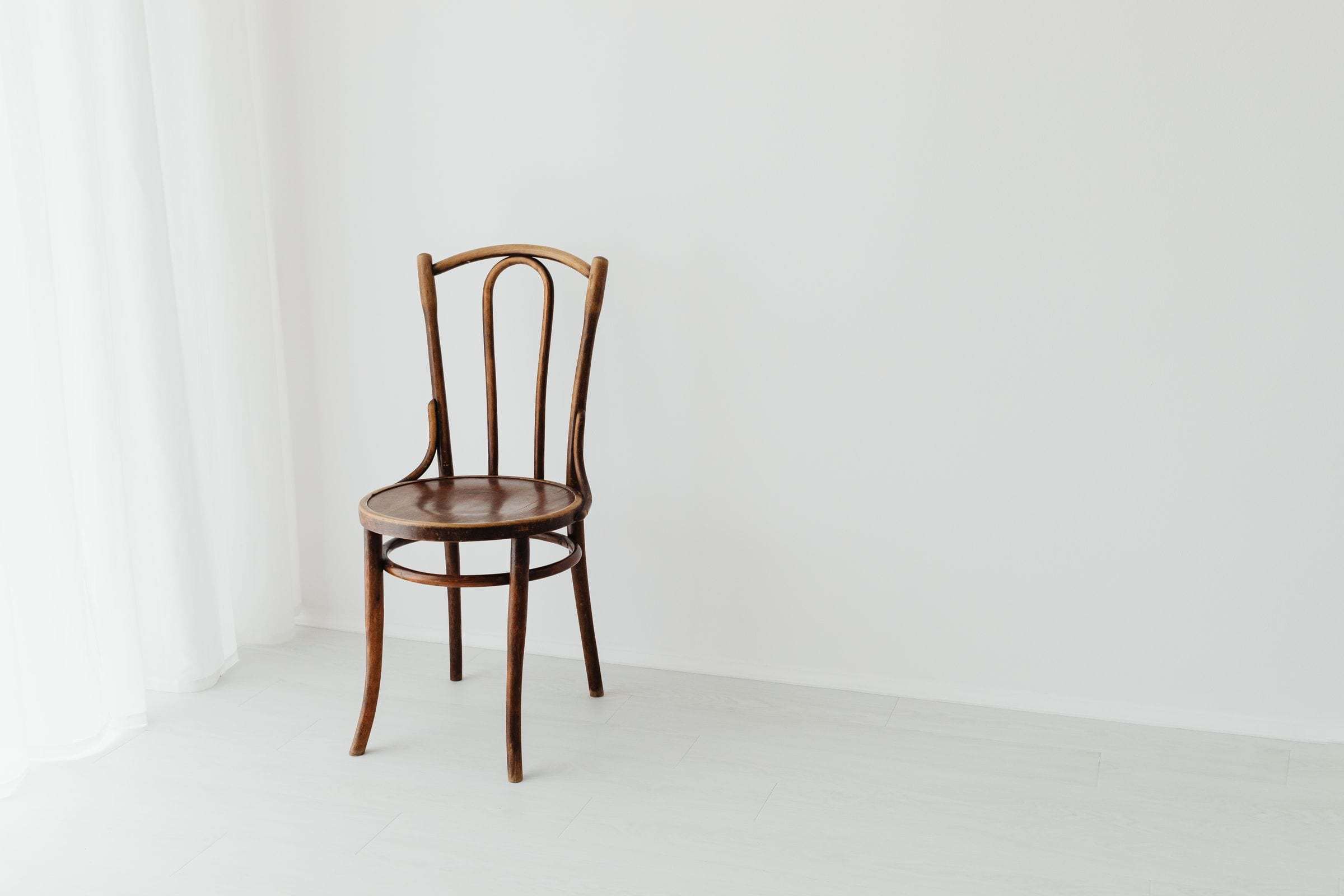 Chaise en bois cintré devant un grand mur fraîchement peint, voilage et lumière douce