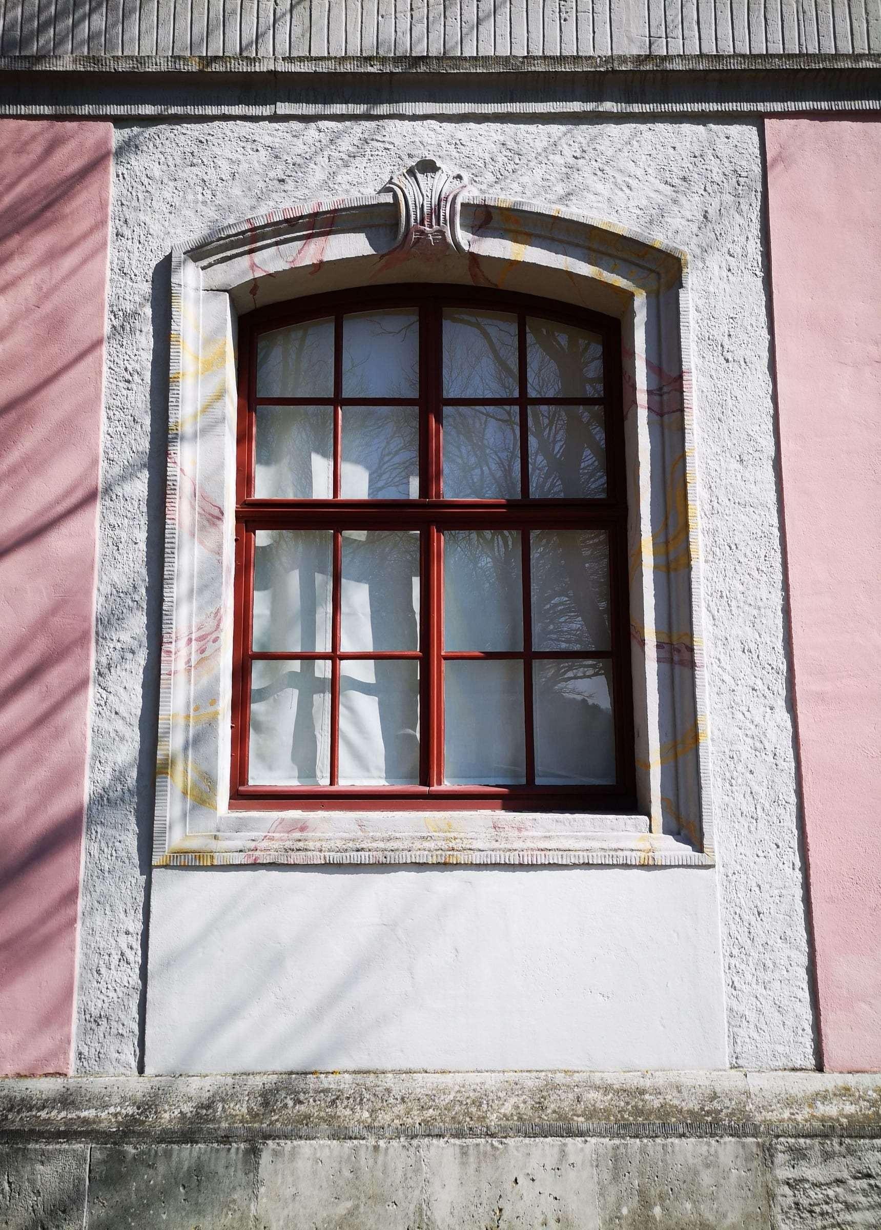 Fenêtre cintrée dans un encadrement mouluré, sur un crépi de façade blanc et rose