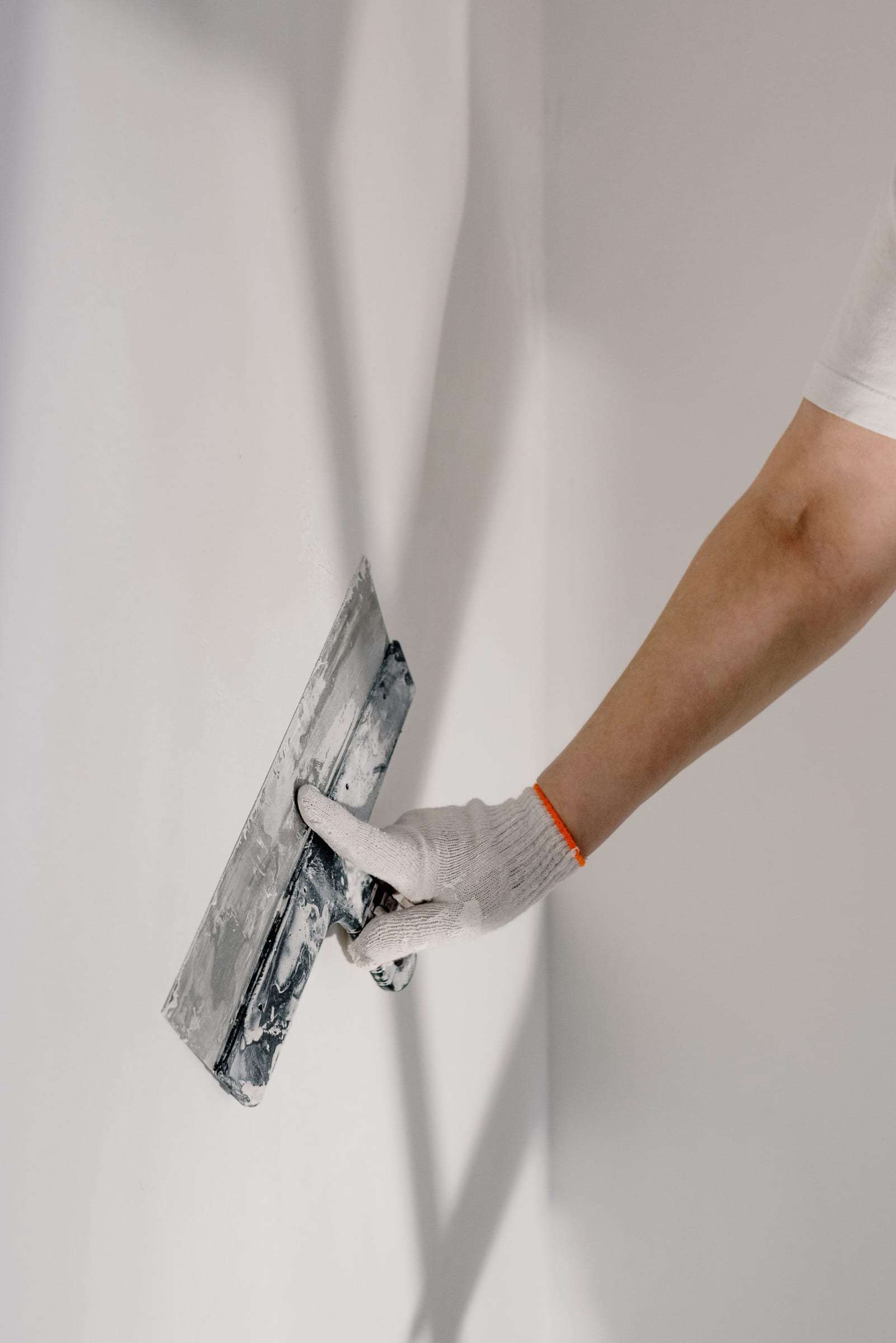 Main gantée lissant un enduit sur un mur en plaques de plâtre